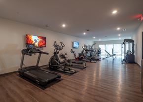 Springdale townhouse for rent - a gym with treadmills and other exercise equipment on a wooden floor at The Row on Merchant Apartments, Springdale, Ohio