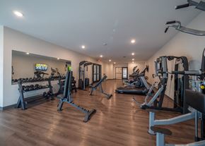 Springdale townhouse for rent - a gym with cardio equipment and weights on a wooden floor at The Row on Merchant Apartments, Springdale, OH