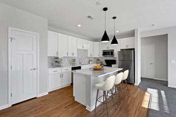A large white kitchen with an island and white chairs