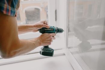 A man drilling into a window with a drill