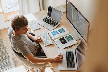 A man sitting at a desk with three laptops and a tablet