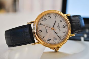A gold watch with a white face and black straps