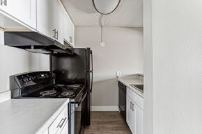 Colorado Springs apartment for rent - an empty kitchen with white cabinets and a black stove and refrigerator