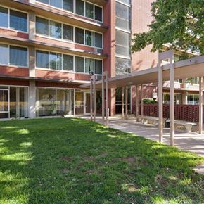 Denver apartment for rent - A building with a red brick facade and a white pergola over a grassy area.