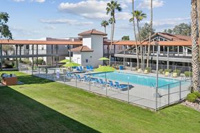 Tucson apartment for rent - A pool surrounded by a fence with chairs and umbrellas.