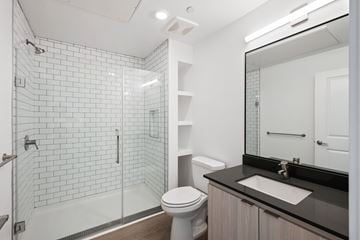 San Diego apartment for rent - A white toilet sits in a bathroom with a black counter top and a walk in shower.