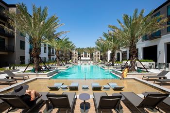 A man sits on a lounge chair next to a pool with palm trees in the background