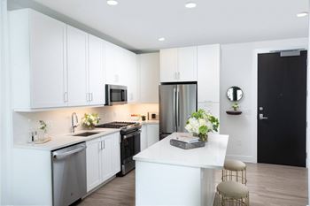 A kitchen with white cabinetry and a white island with two stools