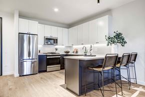 Chicago apartment for rent - A modern kitchen with a stainless steel refrigerator, microwave, oven, and bar stools at Windsor North + Vine 633 W North Ave, Chicago, IL 60610.
