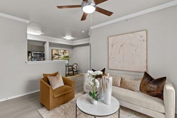 Austin apartment for rent - A living room with a brown armchair, a white couch, and a round table with a vase of flowers on it.