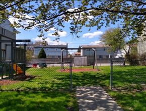 Southfield apartment for rent - A playground with a swing set and a slide is surrounded by a fence and trees.