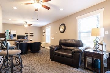 Olathe apartment for rent - A living room with a black leather couch and a ceiling fan.