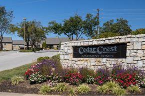 Overland Park townhouse for rent - The Cedar Crest Apartments sign displayed in front of a stone wall, surrounded by flowers and landscaping.