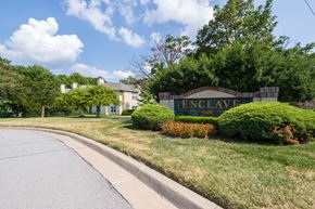 Overland Park apartment for rent - The Enclave at Town Center sign is displayed in front of a stone wall, surrounded by flowers and landscaping.
