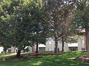 Omaha apartment for rent - Side view of an apartment building with lush green trees in the Muirfield Apartments complex.