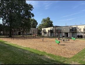 Lawrence townhouse for rent - Playground with green swing set and sandbox at Park 25 Apartments surrounded by open outdoor space.
