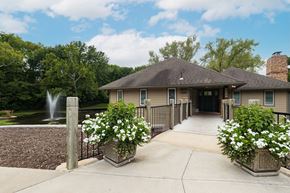 Kansas City townhouse for rent - A charming Tanglewood building with a fountain on the left side and colorful flower beds in pots in the foreground. A bridgeway leads towards the building.