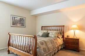 Kansas City townhouse for rent - A cozy Tanglewood Model Unit Bedroom with beige walls features a comfortable bed, a nightstand with a lamp on the right side, and wall art adding a touch of personality to the left wall.