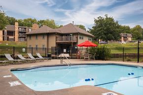 Kansas City townhouse for rent - The Tanglewood swimming pool is located in the backyard of the apartment complex, complete with lounge chairs, a red umbrella on a table with chairs, inviting residents to relax and enjoy the summer.