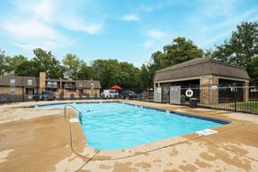 Kansas City townhouse for rent - The Tanglewood swimming pool, nestled within the apartment complex, offers a refreshing escape for residents. Enjoy the poolside amenities, including lounge chairs, a table with chairs, and a red umbrella, with the backdrop of the surrounding apartments.