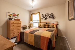 Kansas City apartment for rent - Cozy bedroom with wood bed and dresser, beige walls, quilted bedding, and natural light.