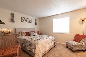 Liberty apartment for rent - Spacious bedroom with a beige upholstered bed, wood dresser, accent chair, and natural light from a window.