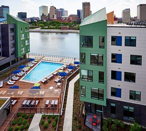 Harrison apartment for rent - A green building with a pool in the foreground and a city skyline in the background.