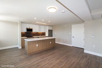 An empty living room with a kitchen in the background