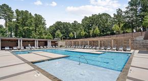 Raleigh apartment for rent - A large outdoor swimming pool surrounded by lounge chairs and trees at Vintage Raleigh West Apartments, Raleigh