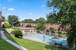 Hyattsville apartment for rent - A pool surrounded by a fence and trees in front of a brick building.