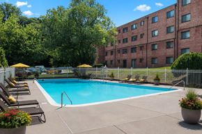 Hyattsville apartment for rent - A pool surrounded by a fence and chairs with trees in the background.