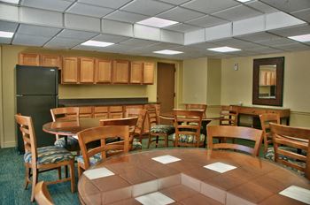 Community room with wood tables and chairs and black fridge