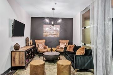 Dallas apartment for rent - A living room with a grey couch, a wooden cabinet, a chair, a table, and a painting on the wall.