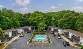 Smyrna apartment for rent - A view of a parking lot with a swimming pool and trees in the background.