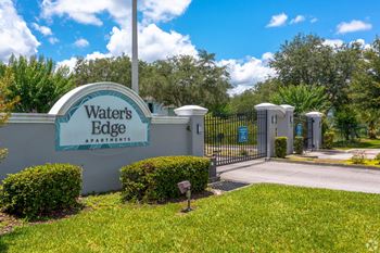 The entrance to waters edge apartments with a blue gate and green grass