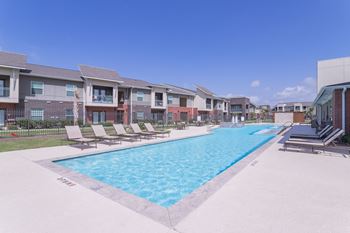 A swimming pool with lounge chairs and apartments in the background