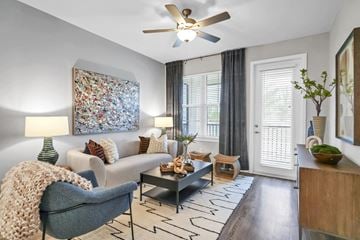 Punta Gorda apartment for rent - A living room with a grey armchair, a white sofa, a coffee table, a ceiling fan, and a large abstract painting on the wall.