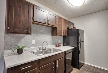 Burleson apartment for rent - A kitchen with a black refrigerator and wooden cabinets.