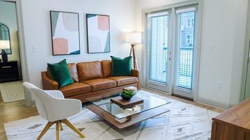 Lafayette apartment for rent - A living room with a brown leather couch, a white chair, and two abstract paintings on the wall.