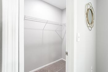 A walk in closet with white walls and a mirrored closet door