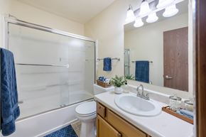 Altoona apartment for rent - A bathroom with a white sink, toilet, and a blue towel hanging on the glass shower door.