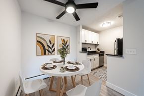 Cincinnati apartment for rent - A dining room with a white table and chairs, a ceiling fan, and a kitchen area in the background.
