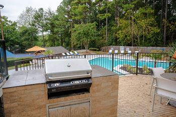 A gas grill on a patio next to a swimming pool