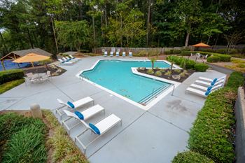 A pool surrounded by trees and a patio with chairs