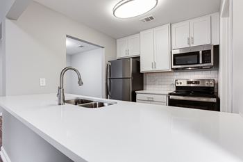 An empty kitchen with white countertops and stainless steel appliances
