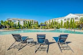 Lakeland apartment for rent - A pool surrounded by chairs and trees with a building in the background.at Century Ariva, Florida, 33812
