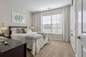 Suffolk apartment for rent - A bedroom with a large bed and a window with blinds.at Century Hampton Roads, Suffolk, VA
