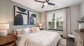 Jacksonville apartment for rent - A bedroom with a large bed, a ceiling fan, and a painting on the wall.