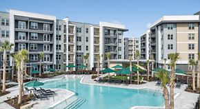 Jacksonville apartment for rent - A large swimming pool surrounded by lounge chairs and umbrellas in front of apartment buildings.