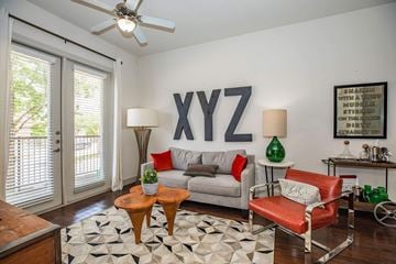 Cedar Hill apartment for rent - A living room with a grey couch, a red chair, a wooden table, and a rug with a black and white pattern.